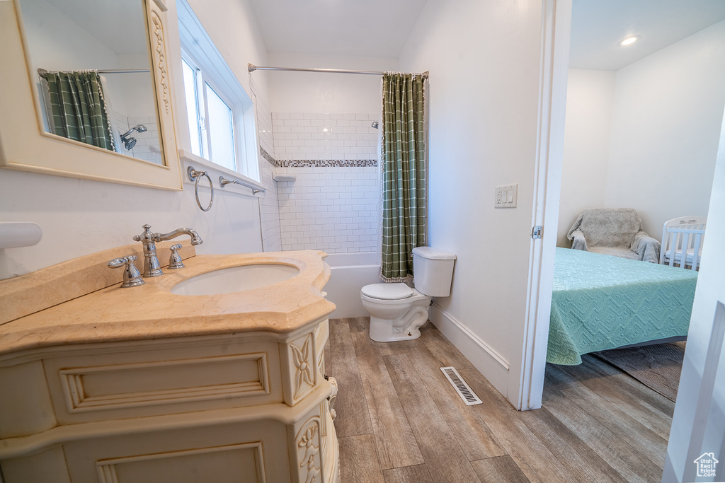 Bathroom featuring wood finished floors, toilet, shower / tub combo with curtain, vanity, and ensuite bathroom