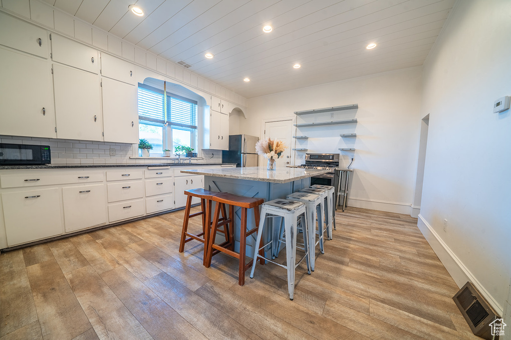 Kitchen with freestanding refrigerator, light wood-type flooring, a kitchen island, black microwave, and a breakfast bar area