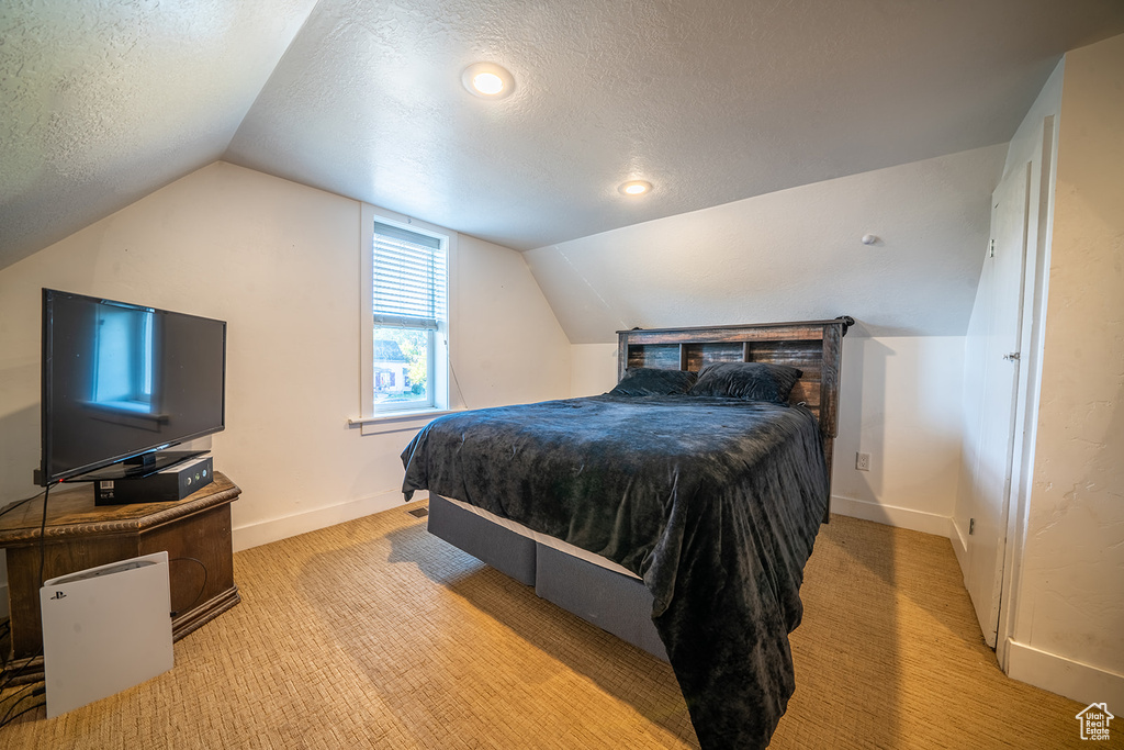 Carpeted bedroom with a textured ceiling, vaulted ceiling, and baseboards