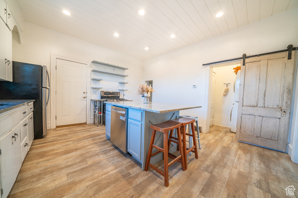 Kitchen featuring stainless steel appliances, light wood-style floors, recessed lighting, a barn door, and a center island
