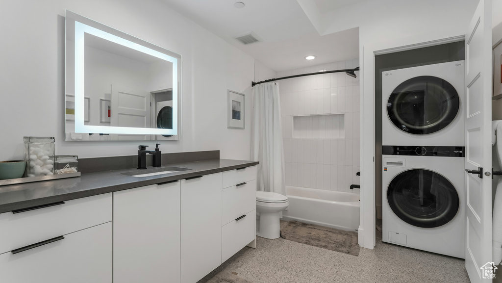 Full bathroom with stacked washer / drying machine, speckled floor, toilet, shower / bath combo, and vanity