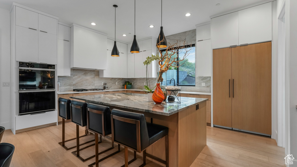 Kitchen with a kitchen island, a kitchen breakfast bar, light wood-style floors, backsplash, and recessed lighting