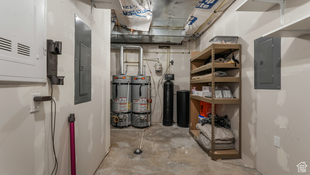 Unfinished basement with strapped water heater, electric panel, and a water softener