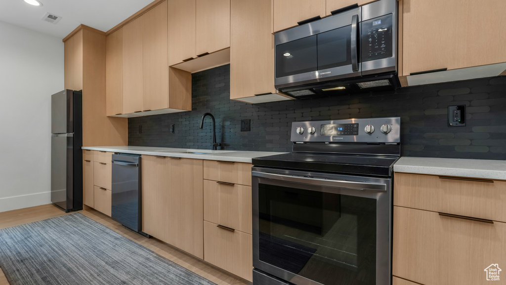 Kitchen with stainless steel appliances, a sink, light countertops, and decorative backsplash