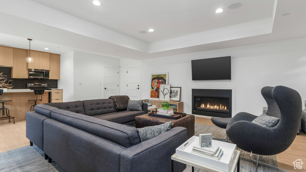 Living room featuring light wood-style floors, a glass covered fireplace, recessed lighting, and a raised ceiling