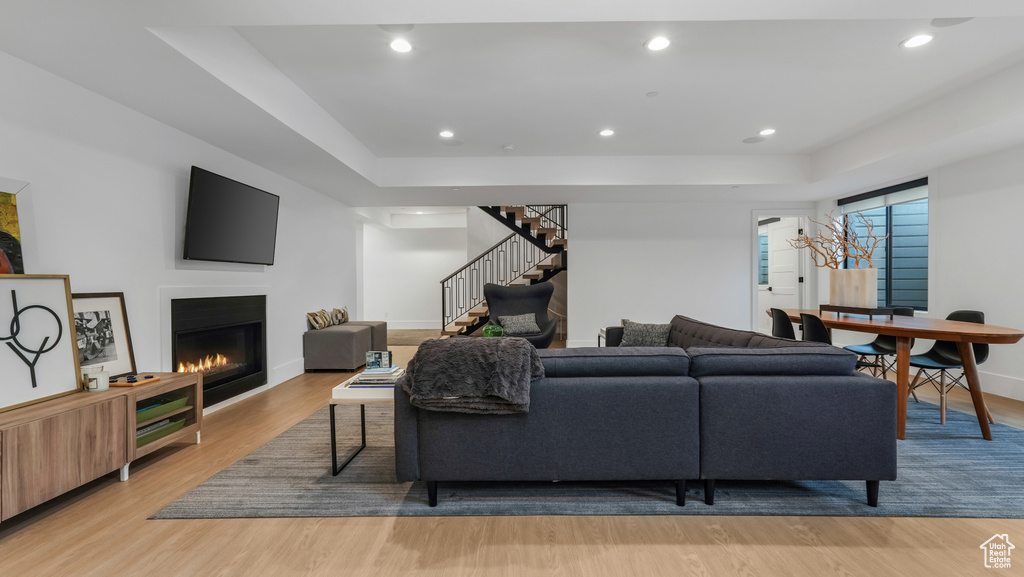 Living area featuring light wood-type flooring, stairs, a glass covered fireplace, baseboards, and a raised ceiling