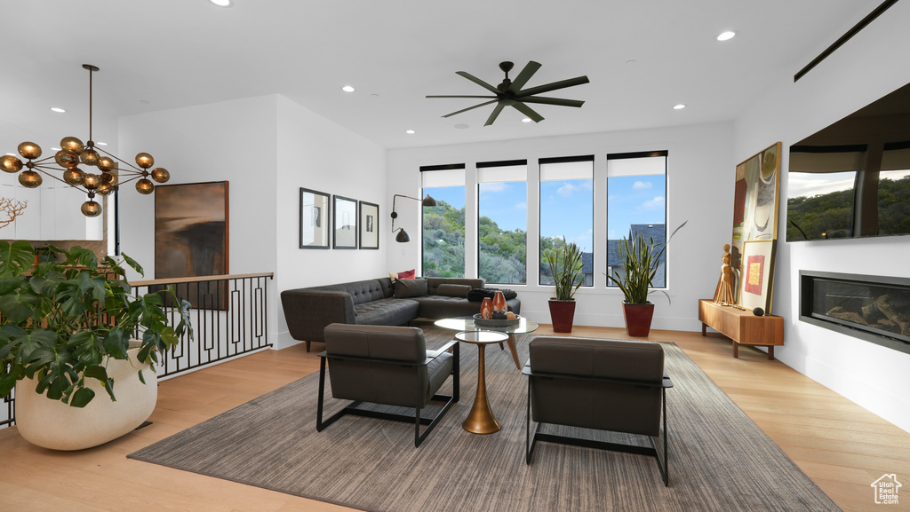 Living area with wood finished floors, recessed lighting, a ceiling fan, a glass covered fireplace, and a chandelier