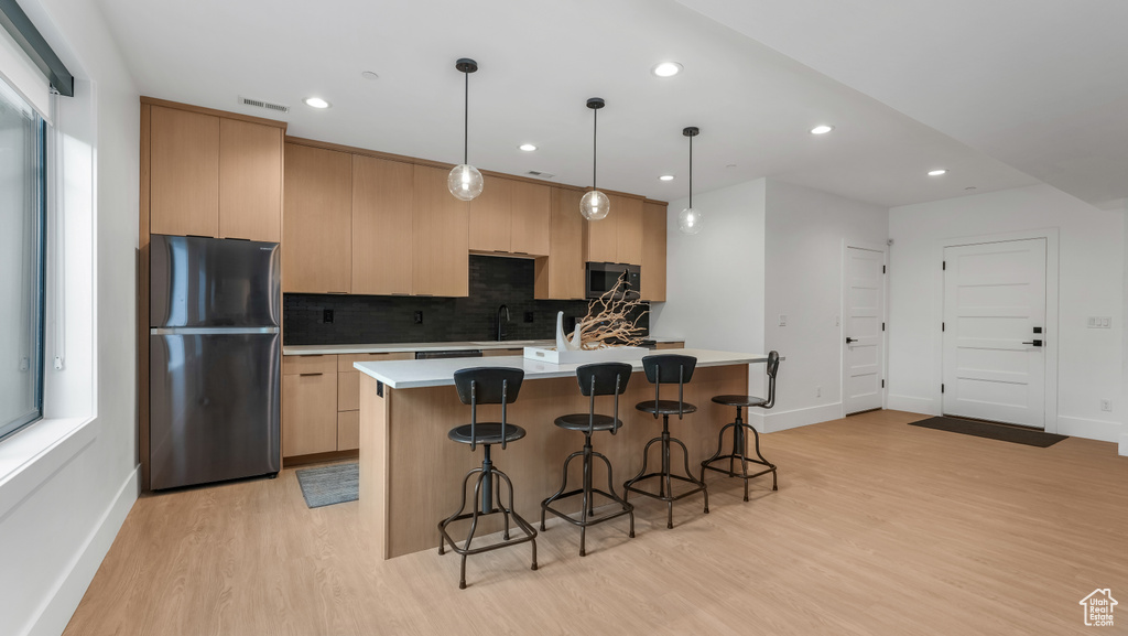 Kitchen with freestanding refrigerator, stainless steel microwave, light wood finished floors, baseboards, and decorative backsplash