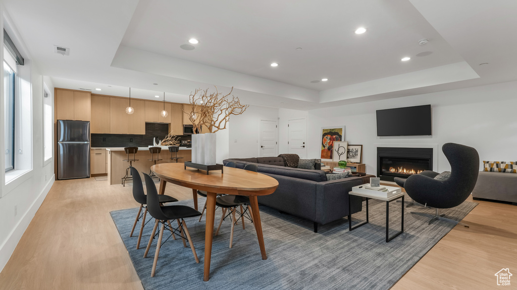 Dining space featuring a raised ceiling, light wood-style floors, plenty of natural light, recessed lighting, and a warm lit fireplace