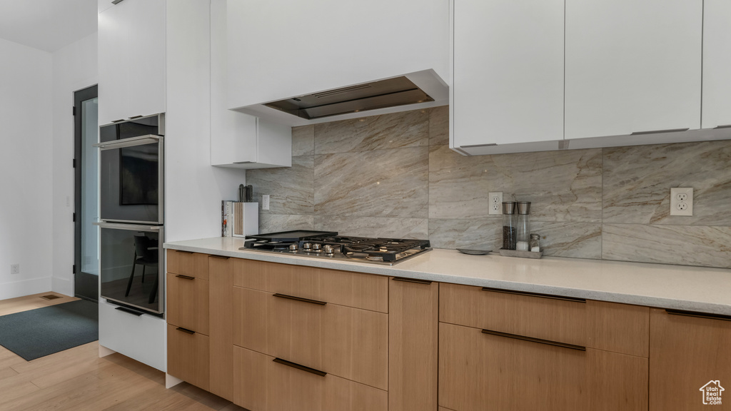 Kitchen featuring stainless steel appliances, light countertops, modern cabinets, decorative backsplash, and light wood-type flooring