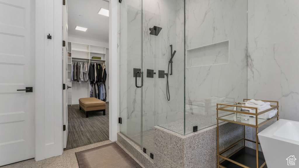 Full bathroom featuring a marble finish shower, a walk in closet, a tub to relax in, a sink, and speckle patterned floor