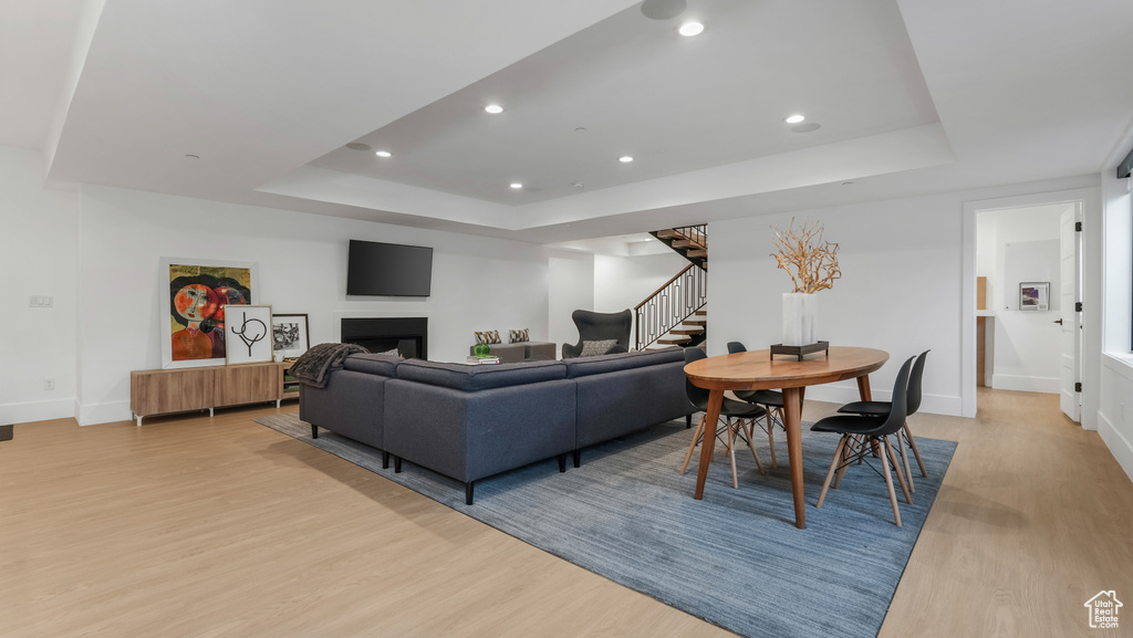Living room featuring a raised ceiling, light wood-style floors, stairs, recessed lighting, and baseboards