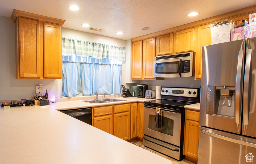 Kitchen with appliances with stainless steel finishes, a sink, light countertops, and recessed lighting