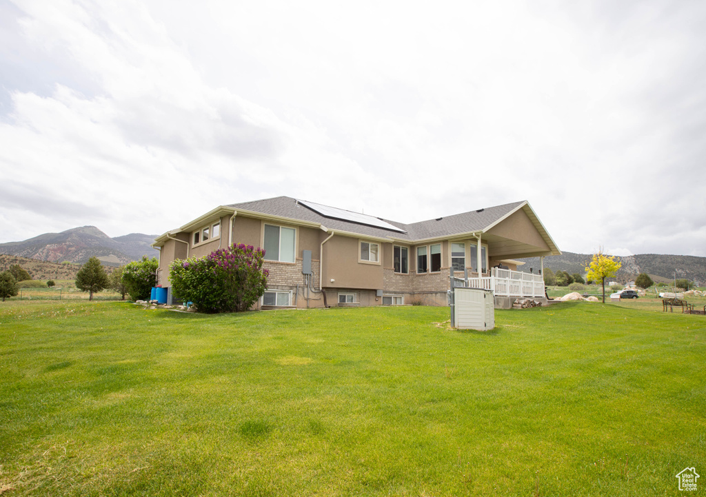 Back of property with roof mounted solar panels, a mountain view, and a lawn
