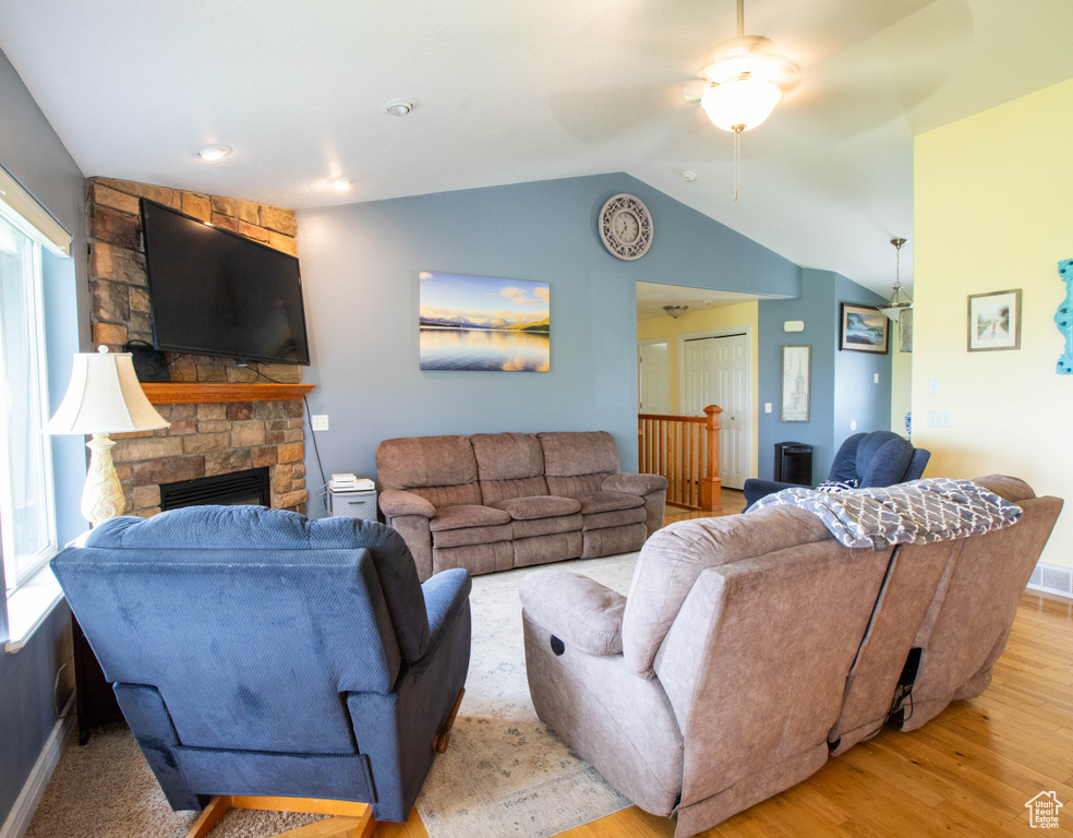 Living area featuring lofted ceiling, light wood-style floors, ceiling fan, a stone fireplace, and plenty of natural light
