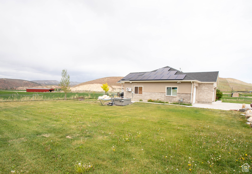 Back of house with roof mounted solar panels, a mountain view, brick siding, and a patio