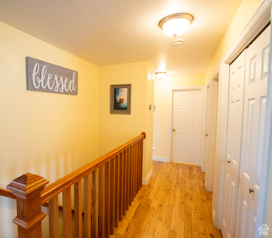 Hallway with light wood finished floors, baseboards, and an upstairs landing