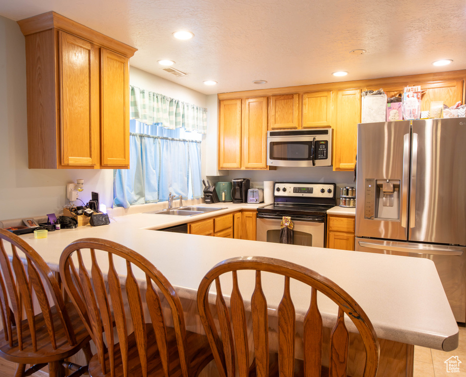 Kitchen featuring stainless steel appliances, a sink, light countertops, a peninsula, and recessed lighting