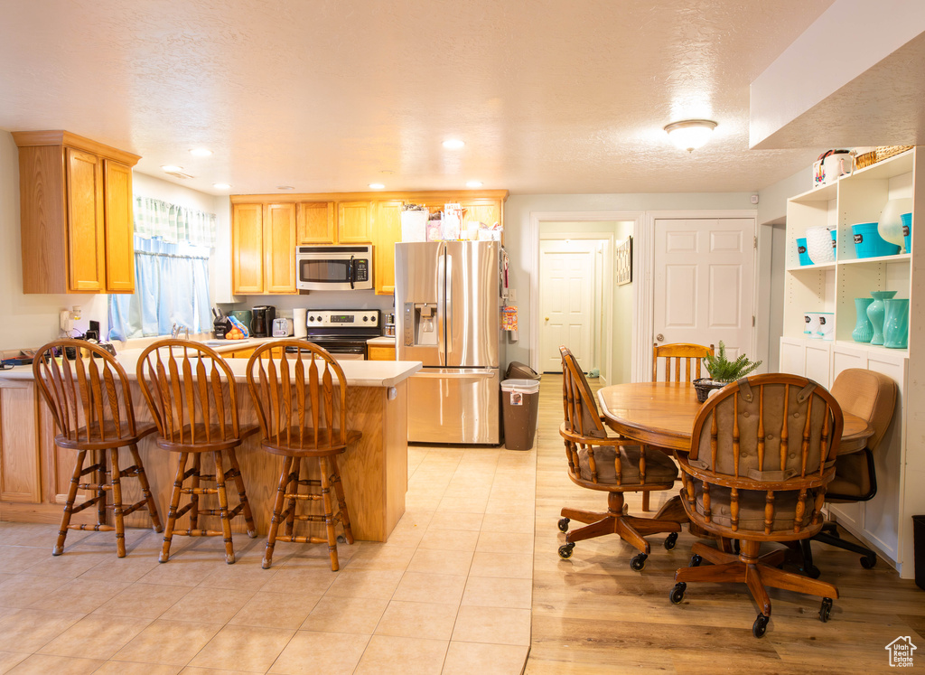 Kitchen with appliances with stainless steel finishes, a peninsula, a breakfast bar, light brown cabinetry, and light countertops