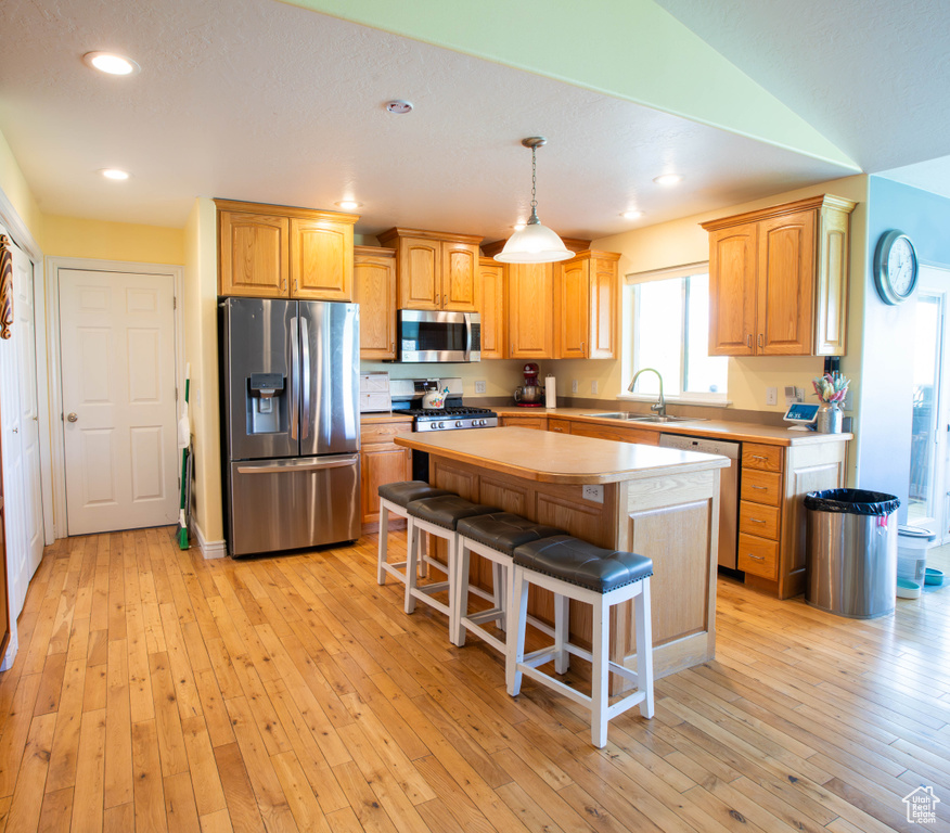 Kitchen featuring stainless steel appliances, a kitchen island, a kitchen bar, light wood-style floors, and recessed lighting