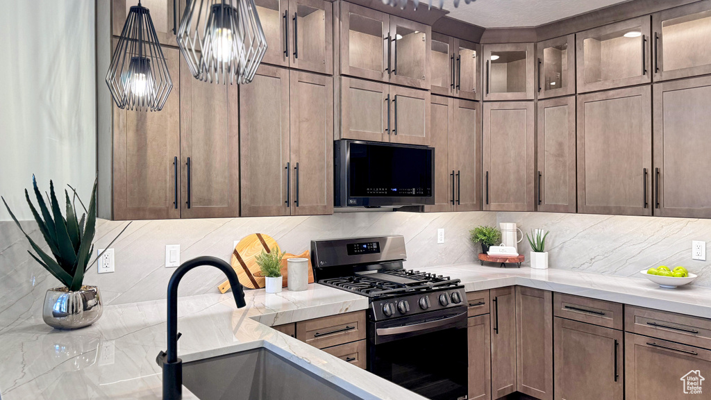 Kitchen with stainless steel gas range oven, backsplash, a sink, glass insert cabinets, and pendant lighting