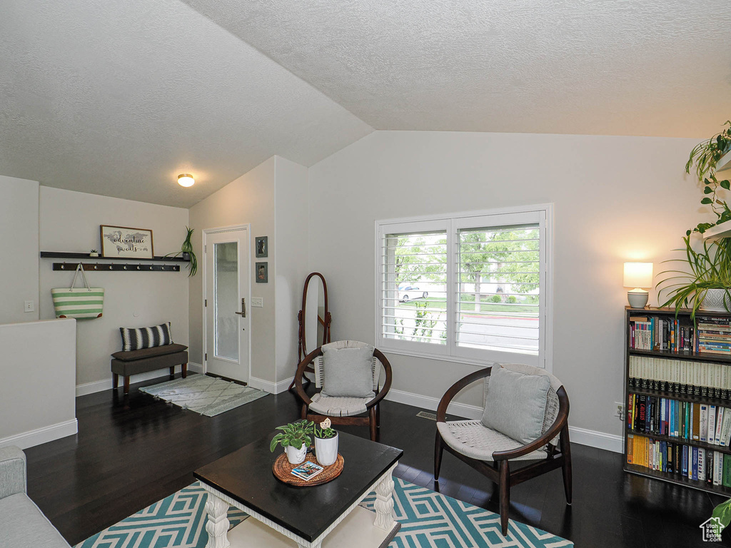 Living area with vaulted ceiling, wood finished floors, a textured ceiling, and baseboards