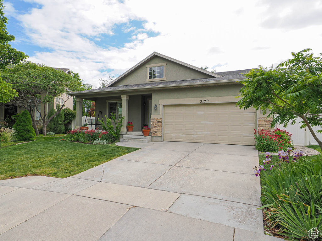 View of front of house featuring stucco siding, a front lawn, an attached garage, concrete driveway, and stone siding
