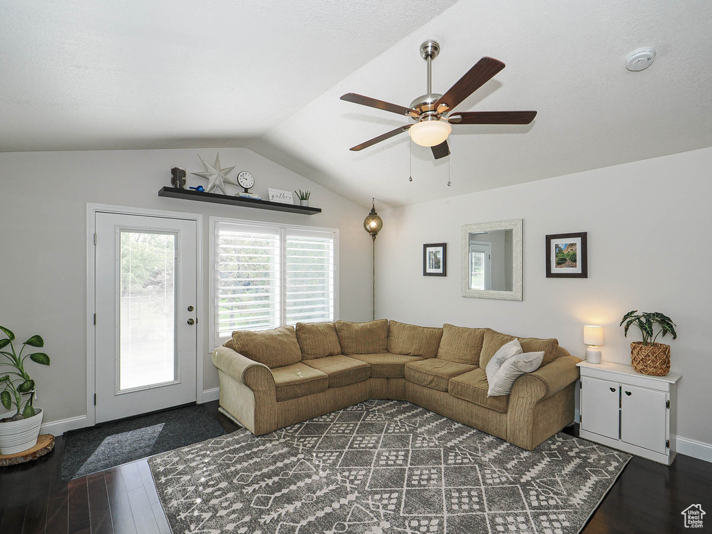 Living area featuring dark wood finished floors, a ceiling fan, baseboards, and vaulted ceiling