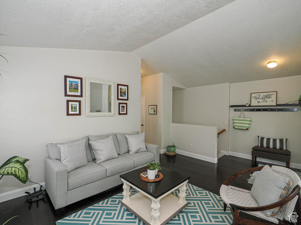 Living area with lofted ceiling, wood finished floors, baseboards, and a textured ceiling