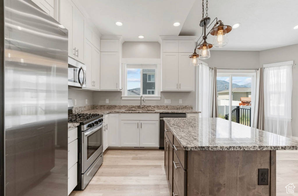 Kitchen with stainless steel appliances, a center island, light wood-style floors, white cabinetry, and a sink