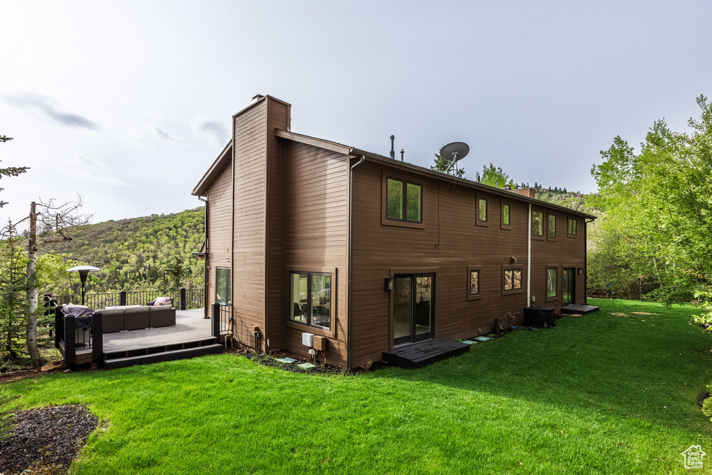 Back of property featuring a chimney, a deck, a lawn, and central AC unit