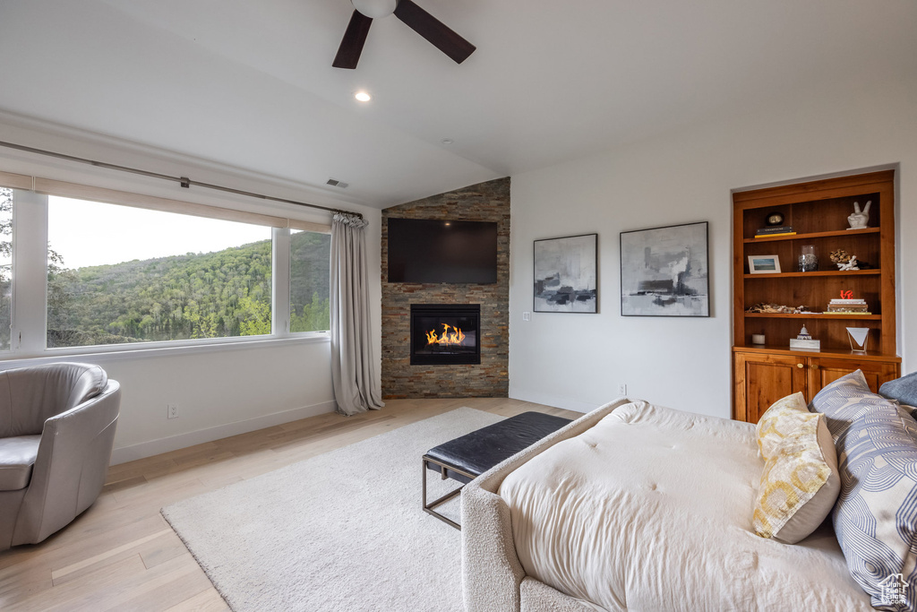 Bedroom featuring vaulted ceiling, a stone fireplace, light wood-type flooring, baseboards, and a ceiling fan