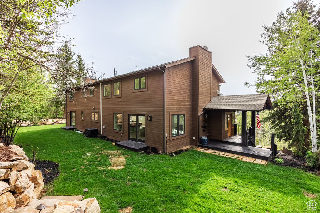 Back of property featuring a chimney, a lawn, cooling unit, and a deck