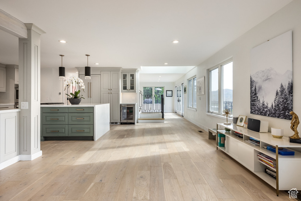 Interior space with green cabinets, beverage cooler, light wood-style flooring, recessed lighting, and hanging light fixtures