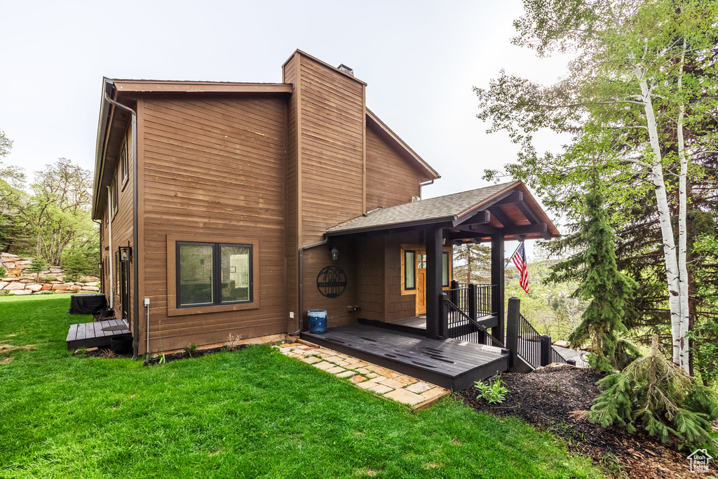 Rear view of property featuring a chimney, a yard, and a wooden deck