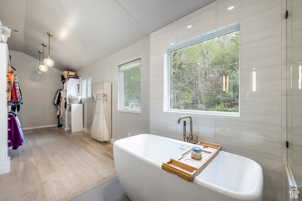Full bathroom featuring wood finished floors, a soaking tub, lofted ceiling, and baseboards