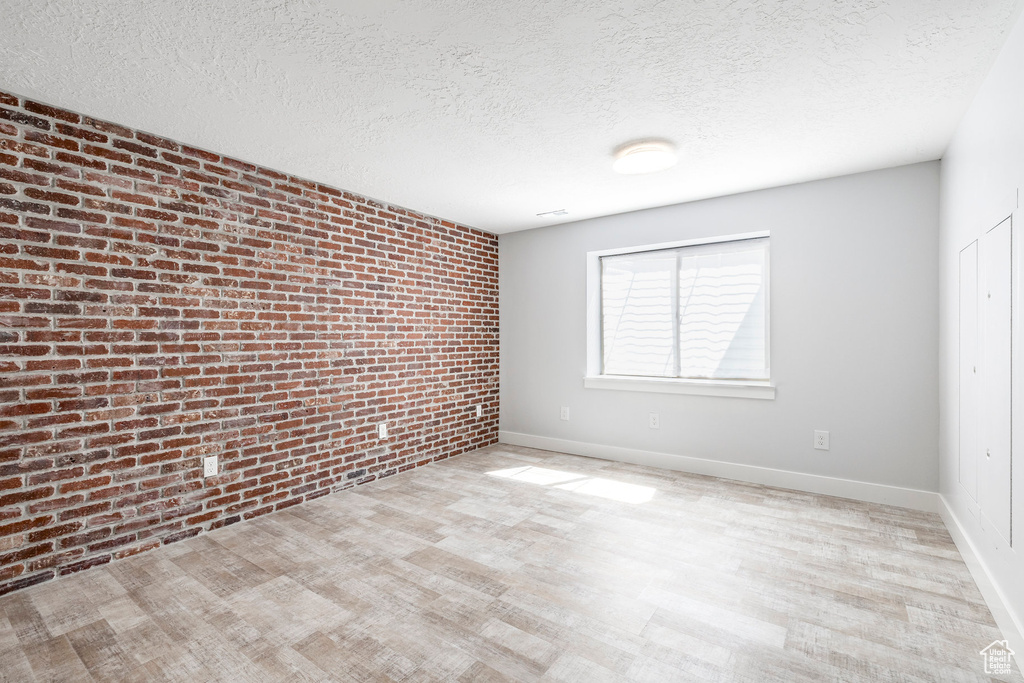 Empty room featuring brick wall, a textured ceiling, light wood finished floors, and baseboards