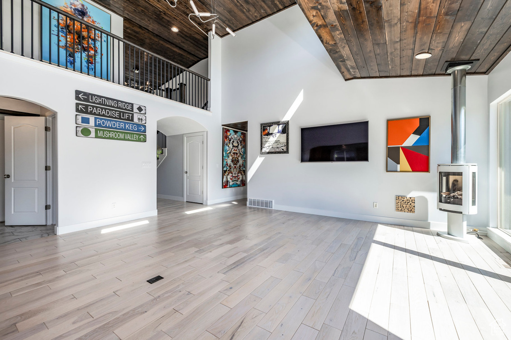 Unfurnished living room featuring wooden ceiling, arched walkways, wood finished floors, baseboards, and a high ceiling