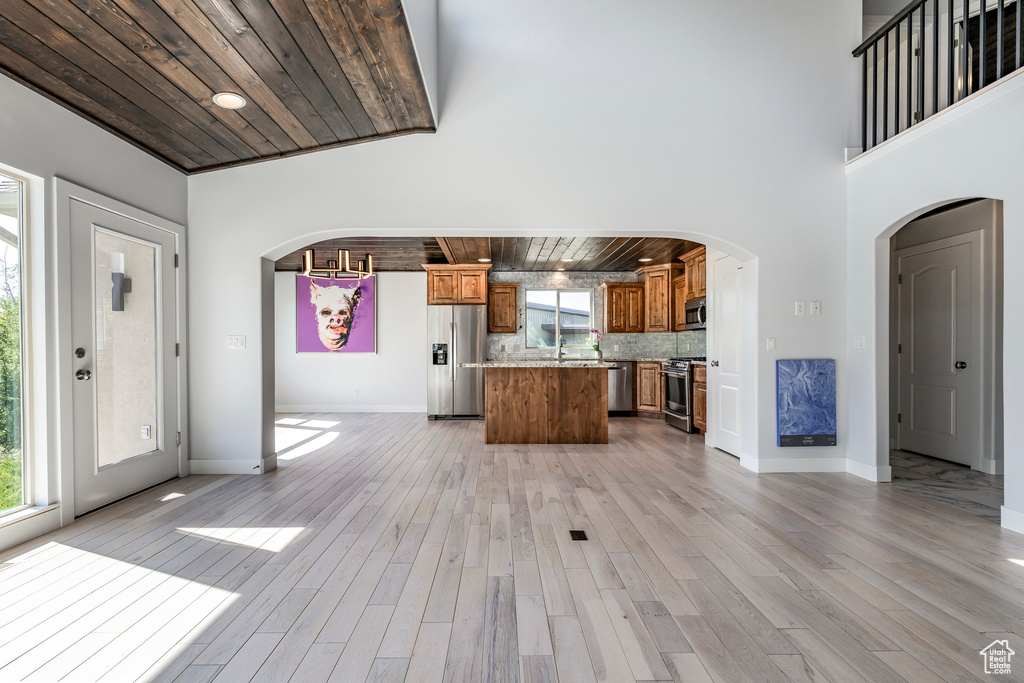 Kitchen with stainless steel appliances, wood ceiling, arched walkways, brown cabinetry, and a kitchen island