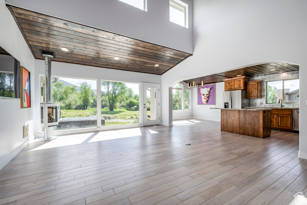 Unfurnished living room with arched walkways, plenty of natural light, wooden ceiling, a sink, and a towering ceiling