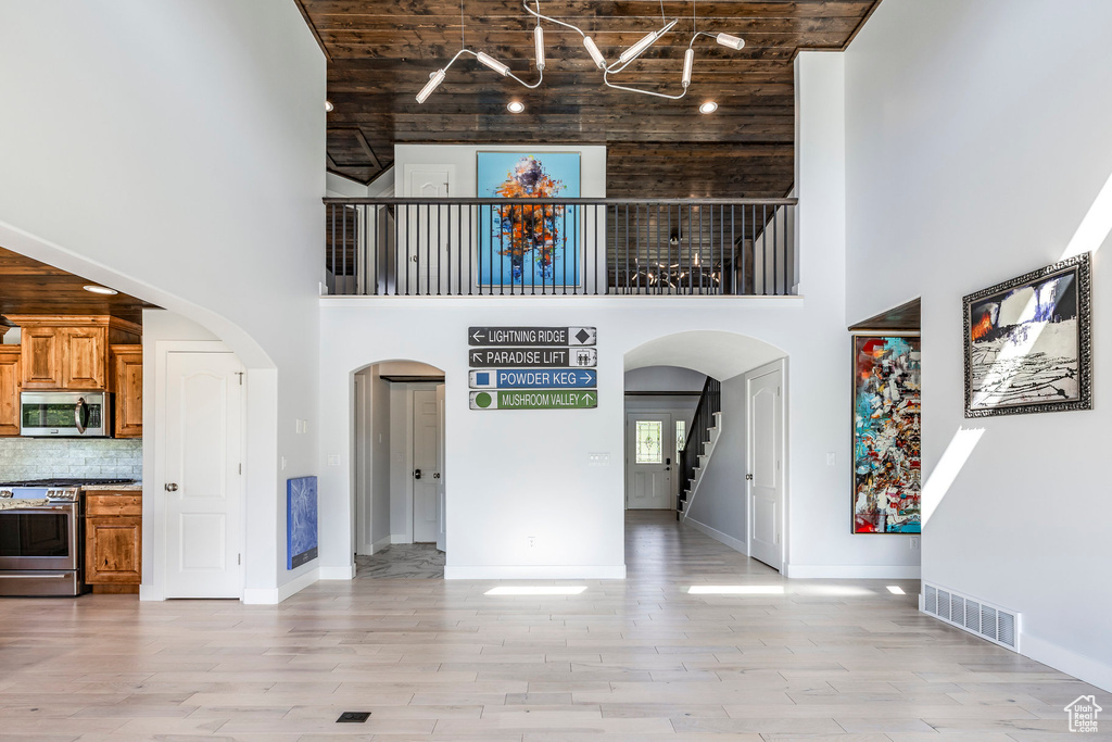 Unfurnished living room featuring a towering ceiling, arched walkways, stairs, baseboards, and light wood-style floors