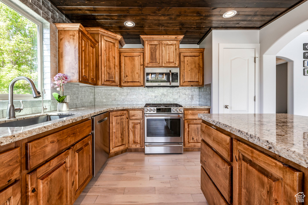 Kitchen featuring appliances with stainless steel finishes, a sink, arched walkways, light wood-type flooring, and light stone countertops