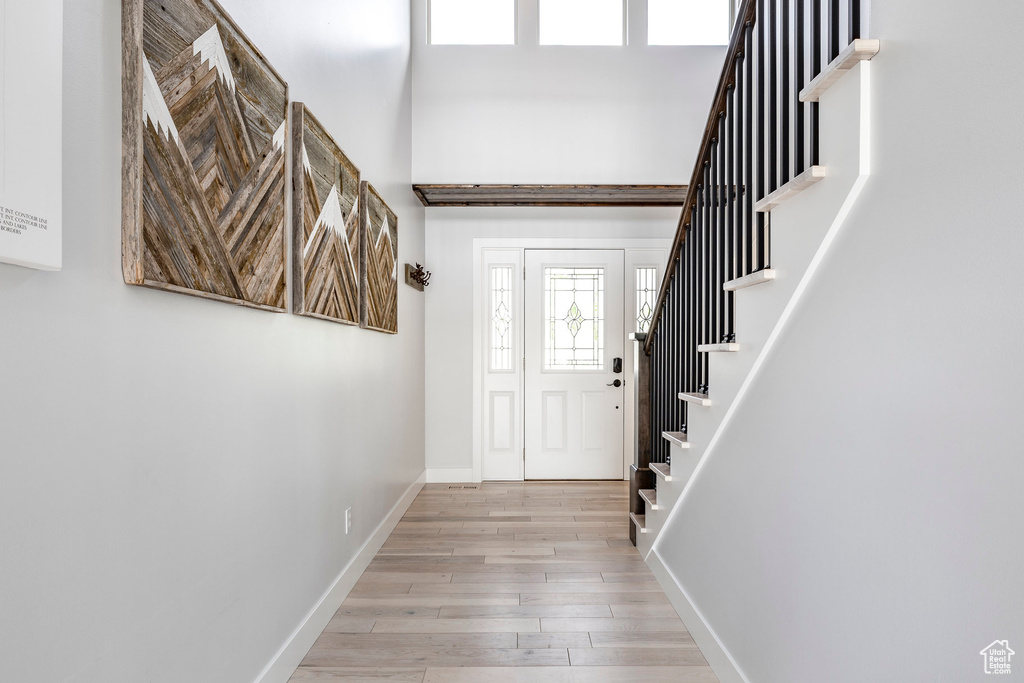 Foyer entrance featuring light wood finished floors, stairway, baseboards, and a high ceiling