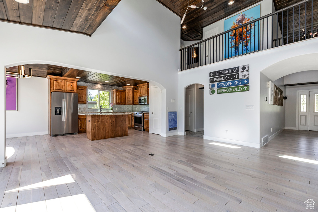 Unfurnished living room featuring arched walkways, wooden ceiling, plenty of natural light, light wood-type flooring, and a high ceiling
