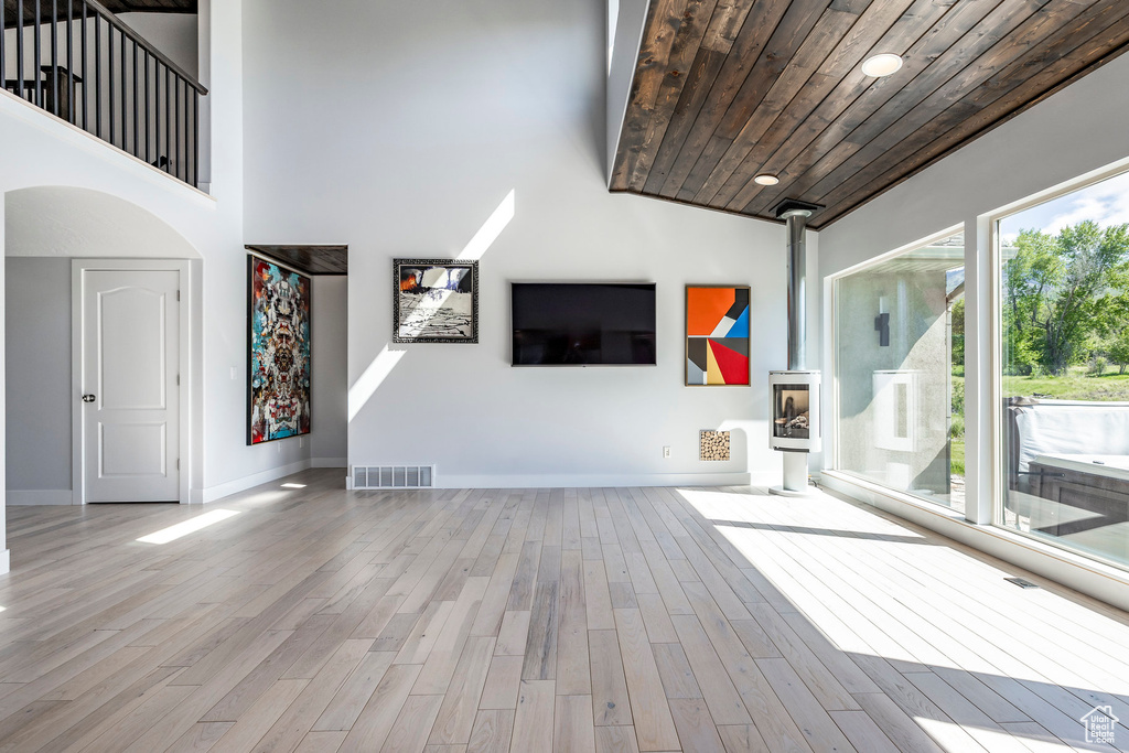 Unfurnished living room with wooden ceiling, a wood stove, high vaulted ceiling, baseboards, and wood finished floors