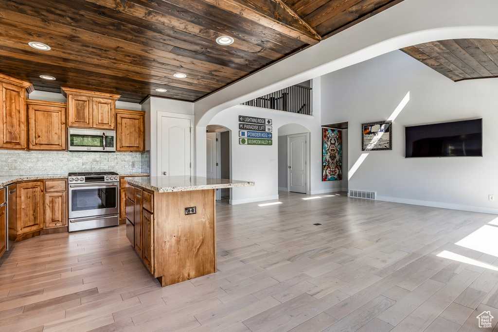 Kitchen with appliances with stainless steel finishes, wooden ceiling, open floor plan, arched walkways, and a center island