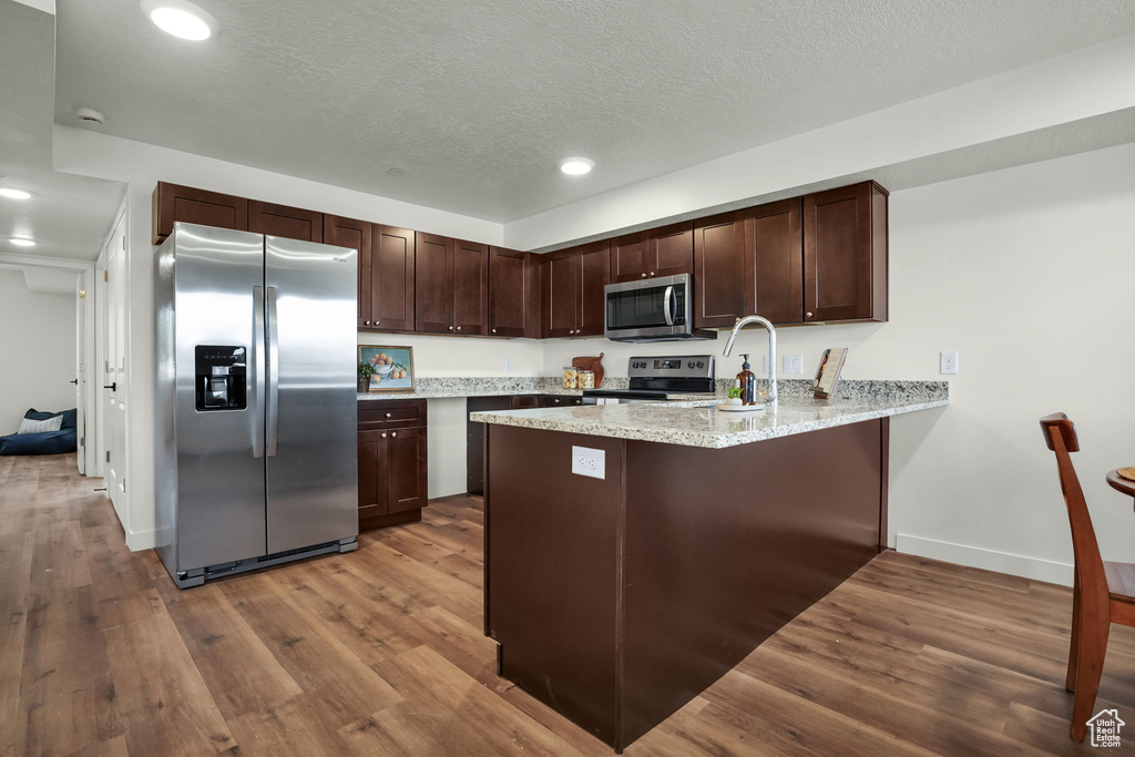 Kitchen featuring appliances with stainless steel finishes, a peninsula, wood finished floors, dark brown cabinets, and baseboards