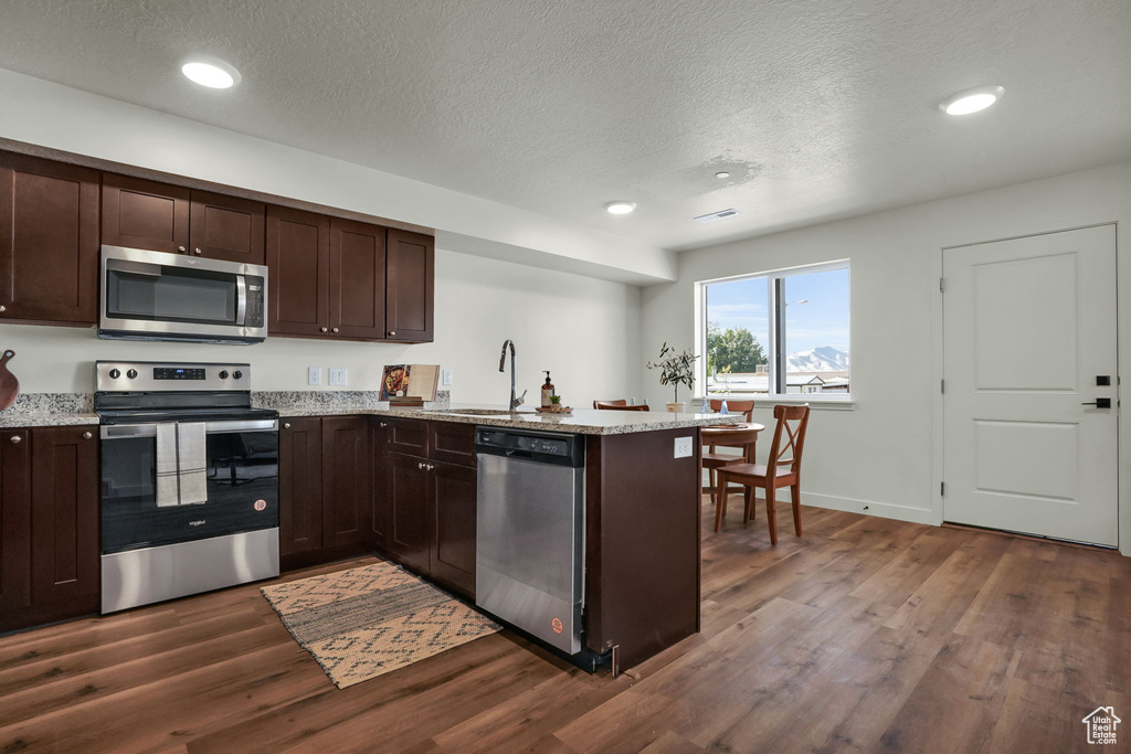Kitchen featuring stainless steel appliances, a sink, dark wood-style flooring, a peninsula, and dark brown cabinets