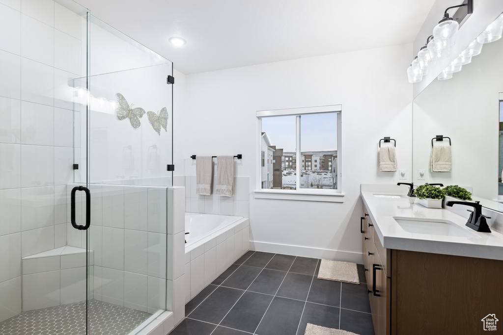 Bathroom featuring tile patterned flooring, a bath, a shower stall, baseboards, and double vanity