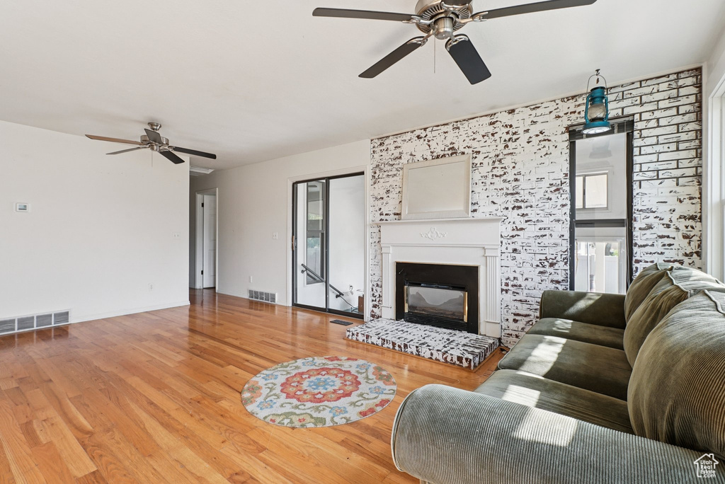 Living area with ceiling fan, a glass covered fireplace, and wood finished floors